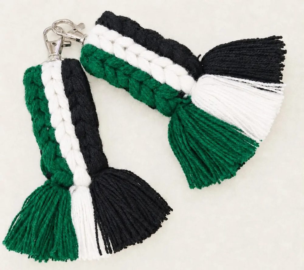 Dos llaveros de macramé con franjas verde, blanca y negra y flecos largos.
